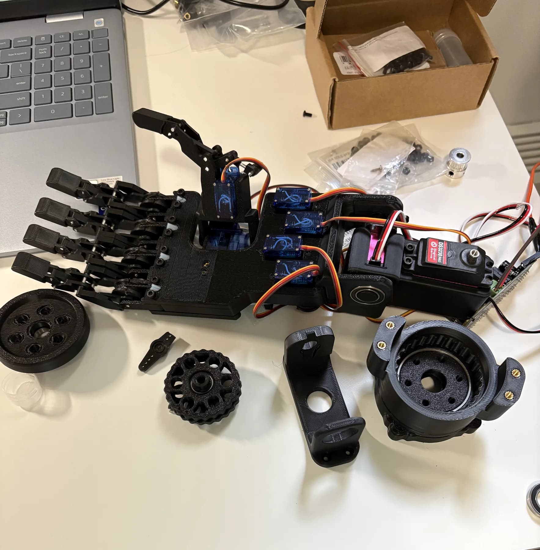 Servo-actuated prototype hand next to a printed cycloidal gearbox